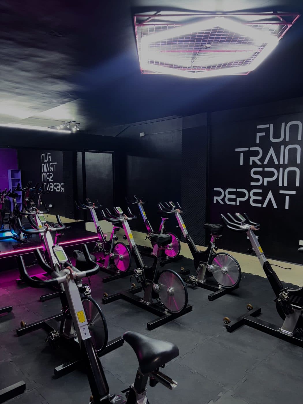 El salón de Bum Bum Spin: bicis en filas, luz neón y el letrero Fun Train Spin Repeat en la pared